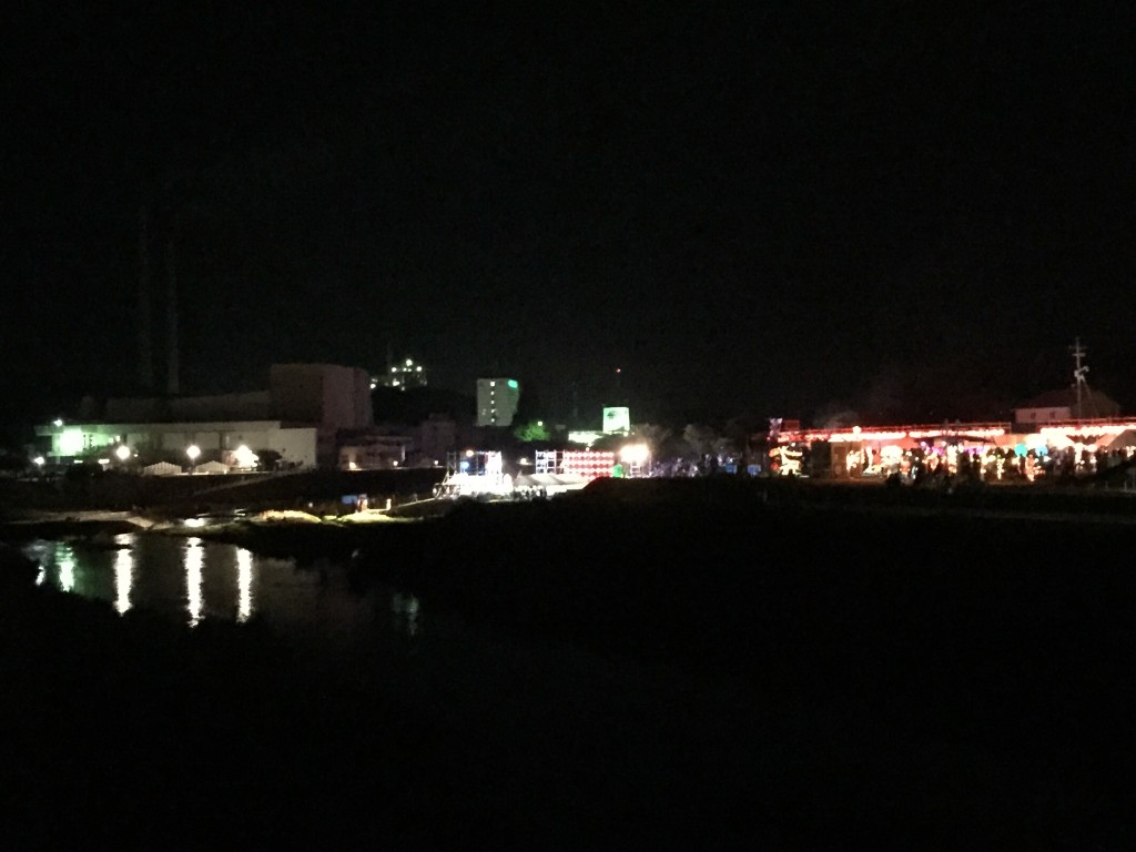 橋からイベント全体を眺める。水面に灯りが反射、背後に美祢市街、さらに向こうに宇部マテリアルズ美祢工場が見えます